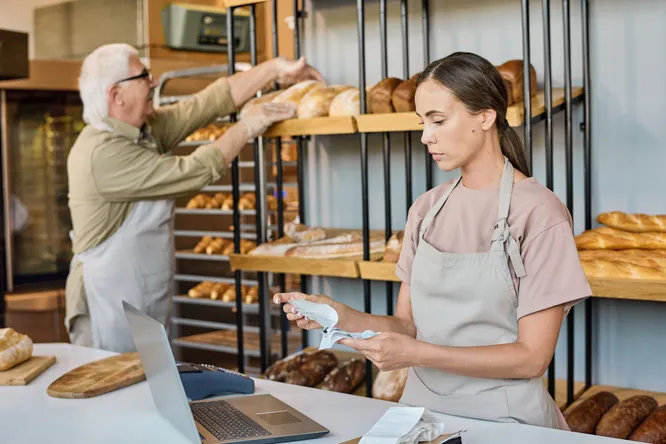 Junge Frau sortiert Rechnungen in einer Bäckerei
